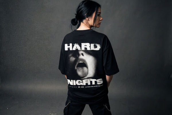 Frau von hinten im schwarzen Oversized T-Shirt mit großem Hard Nights Rückenprint – Techno- und Rave-Streetwear